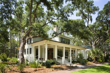 A white house with a darker green roof is done in the Low Country style, including a sitting porch.