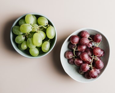 A light blue small bowl filled with green grapes next to a slightly larger light blue bowl of red grapes on a white surface.