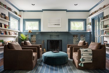 A living room with four dark brown chairs, a blue ottoman, blue rug, and blue accent wall.