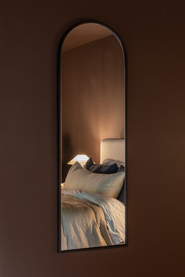 Bedroom wall detail with arched mirror on top of chocolate brown wall paint by Benjamin Moore