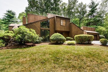 Lauren Liess's 1970s contemporary house is shown with wood siding and a large garden of shaped topiaries