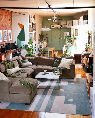 A living room with a brown-gray sectional, graphic-patterneed green and beige rug.