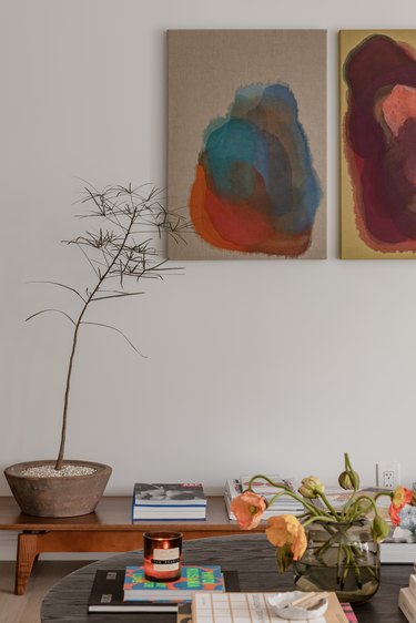 A vintage bench in living room displaying book collection with two works of art hanging above