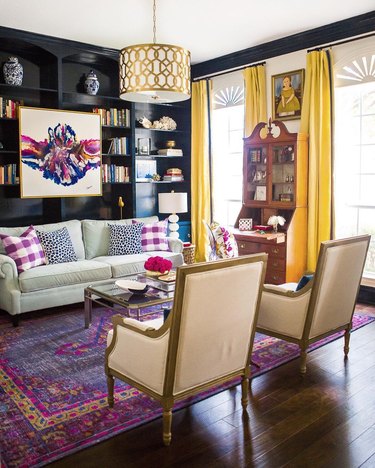 Jewel-toned living room with yellow curtains, navy walls, and a purple rug.