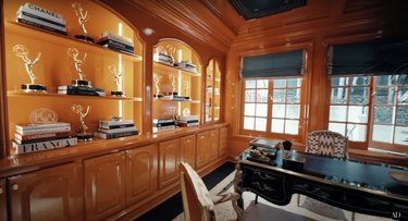 RuPaul's orange office filled with Emmy awards on a built-in bookcase.