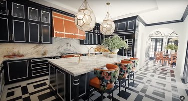 RuPaul's kitchen with a bold orange La Cornue French hood and oven and black cabinetry.