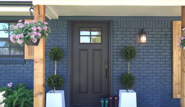 Navy blue brick home exterior with black window trim, black front door and light wood accents.