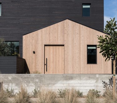 Modern home exterior with black and natural wood siding, black windows.