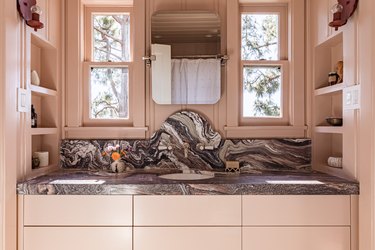 A light pink bathroom vanity with trim the same color as the walls and a dark gray and white marble countertop sink.