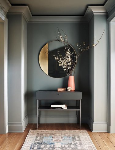 A foyer with a table, mirror, vase with flowers, and gray trim the same color as the walls.