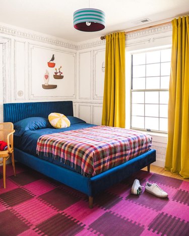 bedroom with yellow curtains, royal blue bed, fuchsia carpet, and plaid bedspread