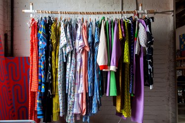 Closet rack with colorful, bold patterned clothing, and a white brick wall.