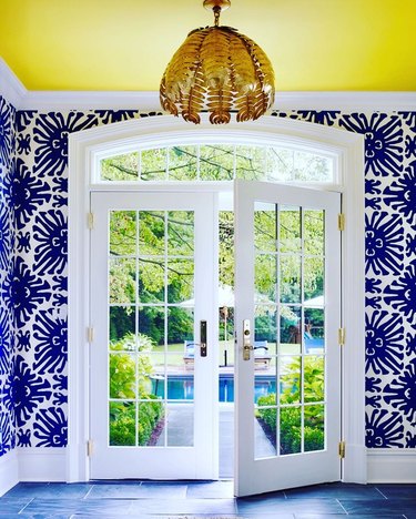 foyer with navy blue and white wallpaper, white trim, yellow ceiling, and brass light fixture