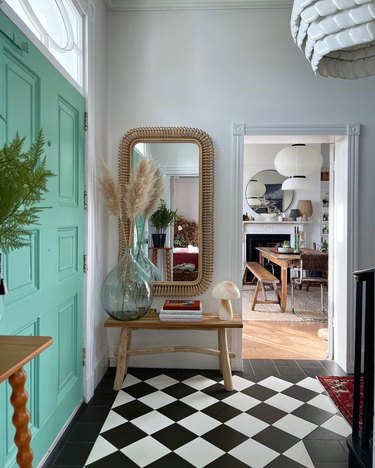 An entryway with a seafoam green door, mirror, and black and white tile on the floor.