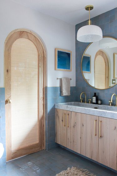 Bathroom with light blue tiles and natural wood door and cabinets.