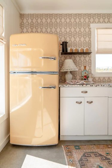 Beige retro refrigerator sitting beside white kitchen cabinets with a speckled terrazzo countertop