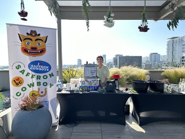 Outdoor photo of a coffee station with a sign that reads "Saffron Cowboy" and a person standing behind the coffee station