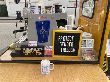 View of a yellow coffee cart with mugs and decor, including a sign that reads "protect gender freedom"