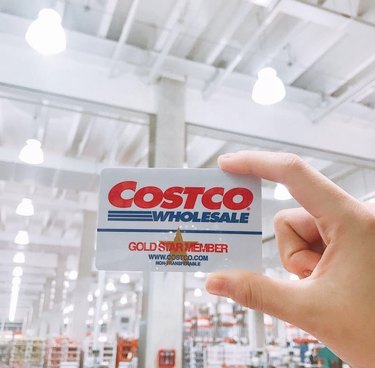 A hand holding a Costco gift card in a Costco warehouse.