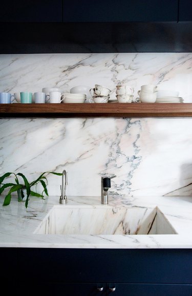 marble kitchen sink, countertops, and backsplash with blue cabinets and wood shelf