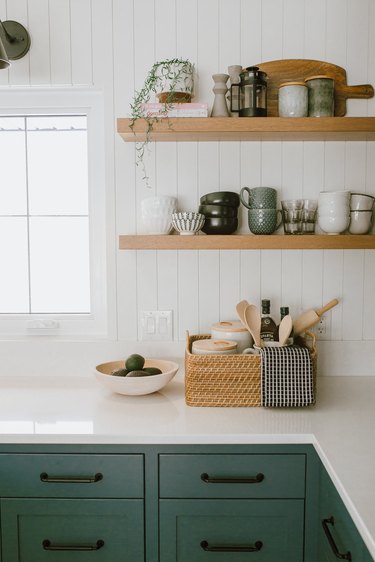 Kitchen with white shiplap backsplash, open shelves, green cabinets.