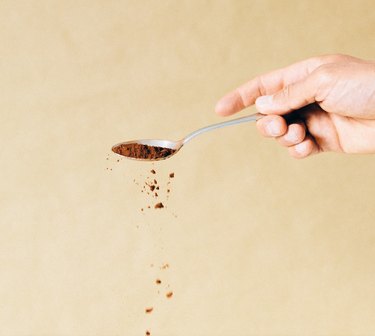 A hand holding a silver spoon that is sprinkling cinnamon powder into the air.