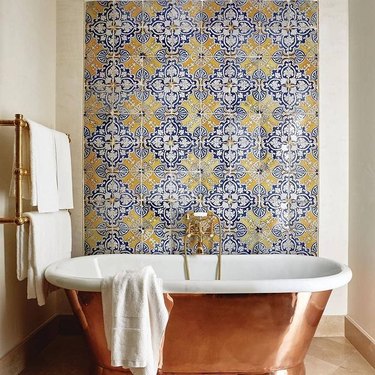 copper bathtub in front of yellow tiled wall