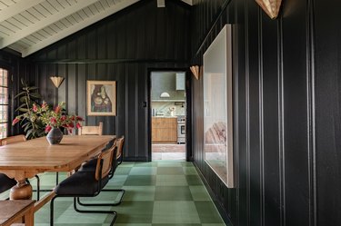 Dining room with a green checkered floor, black panel walls, gold Art Deco sconces, wood-cane dining furniture.