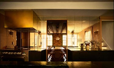 Kitchen with mirrored backsplash, brass hood, and soapstone countertops