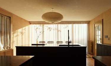 A wall of windows overlooks the kitchen with walls covered in burlap