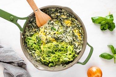 Adding spiralized summer squash to spinach artichoke mixture