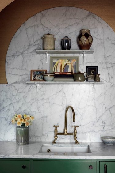Art deco kitchen with marble backsplash, brass sink faucet and green cabinets.