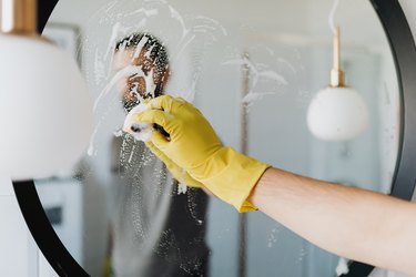 A person wearing a yellow glove and cleaning a mirror.