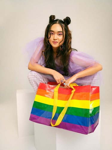 A person crouching holding a rainbow bag