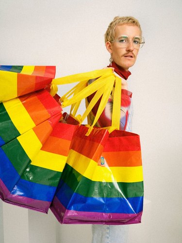 A person holding four rainbow bags over their shoulder