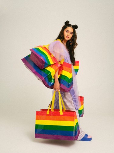 A person standing while holding many rainbow bags