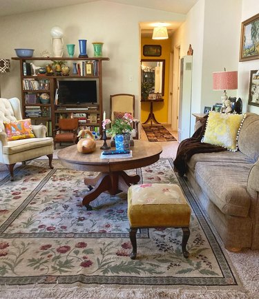 living room with botanical-print rug layered over carpet