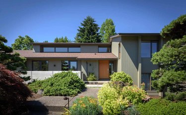 A 1970s split level home with an orange door and a lot of green landscaping in the front