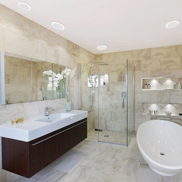 Recessed lighting in a tan bathroom with a glass shower and freestanding tub