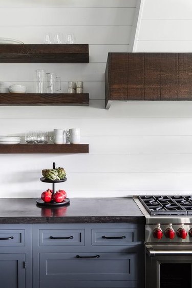 Blue farmhouse kitchen features a shiplap range hood above leathered black granite countertops and blue cabinets with oil rubbed bronze pulls