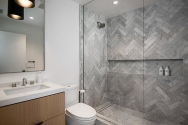 A large glass shower with herringbone tile and recessed lighting in the ceiling