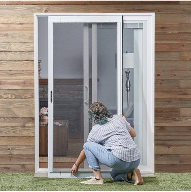 Woman kneeling in front of sliding curtain screen door as she installs it