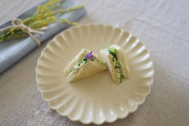 Two triangular cucumber sandwiches on a plate garnished with purple flower