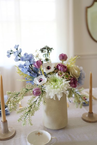 Floral centerpiece in white vase with with blue, white and lilac flowers