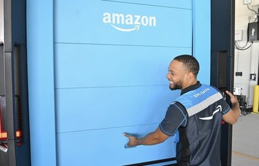 An Amazon worker smiling behind the back of a blue Amazon delivery truck.