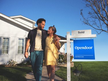 couple with opendoor sold sign in front of their home