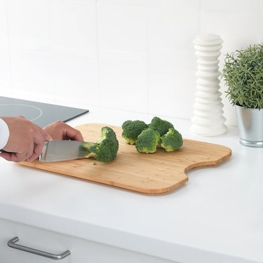 chopping board with broccoli and person holding knife