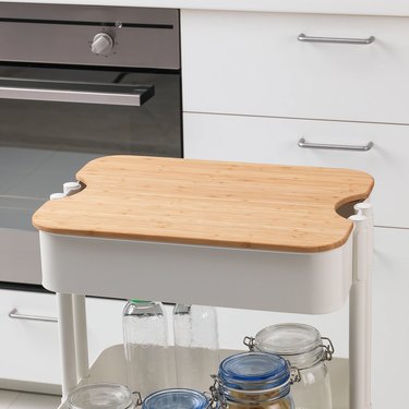 utility cart with chopping board near oven and kitchen drawers