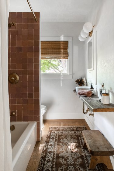 Bathroom with ceramic tile, wood vanity, rug, wood floors, globe vanity lights, bamboo blinds.