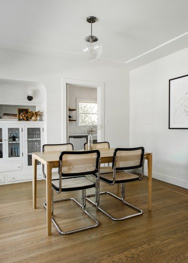 Dining room with wood floors, table, chairs, glass globe pendant, built-in cabinet.